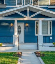 Dieses Haus beeindruckt durch seine himmelblaue Fassade und das hübsche Vordach aus weißem Holz. Eine grüne Fläche und ein Weg führen zur Eingangstür.